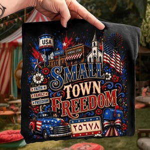 Peut inclure: Un t-shirt noir avec une impression graphique portant le texte "SMALL TOWN FREEDOM". Le motif comprend un château d'eau marqué "USA", un magasin général, une église, un drapeau américain, un camion bleu étoilé et une boîte aux lettres.