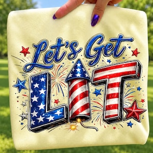 以下が含まれることがあります： 淡い黄色のTシャツで、青い文字で「Let's Get」と書かれています。「LIT」という単語は、赤と白のストライプと青い星柄のコーンを持つ花火のロケットとしてデザインされています。デザインには赤と青の星と花火の爆発が含まれています。