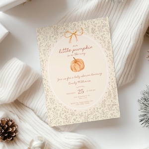 May include: A rectangular baby shower invitation card featuring a cream background with a delicate brown floral pattern. The center oval contains a watercolor pumpkin illustration, a bow, and text reading: our little pumpkin is on the way.