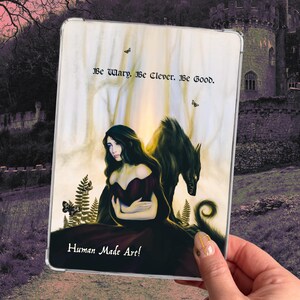 May include: A tablet case featuring a fantasy illustration of a woman in a dark red dress with a wolf. The case has the text "Be Wary. Be Clever. Be Good." and "Human Made Art!"