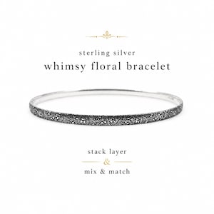 May include: A thin sterling silver bangle bracelet featuring an intricate, dark-toned floral pattern engraved across its surface. The text above reads sterling silver whimsy floral bracelet, and the text below reads stack layer & mix & match.