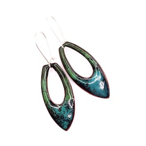 May include: A pair of handmade, open-oval earrings. The earrings feature a gradient of green and teal enamel with a speckled pattern. The earrings are suspended from silver-colored ear wires.
