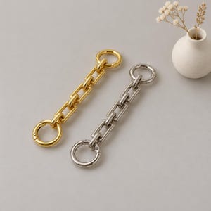 May include: Two metal chain extenders, one in a polished gold tone and one in a polished silver tone. Each extender features a series of rectangular links connected to a circular spring-loaded clasp at both ends for secure attachment.