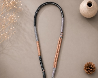 May include: A long, flexible lanyard or strap featuring a multi-colored braided cord design. The cord incorporates segments of black, grey, and tan colors, with silver-toned metal rings attached to both ends for secure attachment purposes.