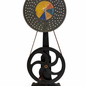 May include: A vintage colour wheel optical toy. It has a large, toothed wheel with a segmented, colourful disc at the centre. A smaller wheel is connected by a belt, all mounted on a black metal stand. A classic optical device.