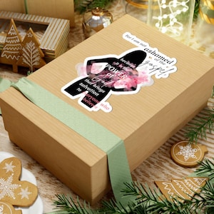 May include: A sticker with the text "For I am not ashamed of the gospel, because it is the POWER of God that brings salvation to everyone who believes." The sticker features a silhouette and pink floral accents, placed on a wrapped gift box.