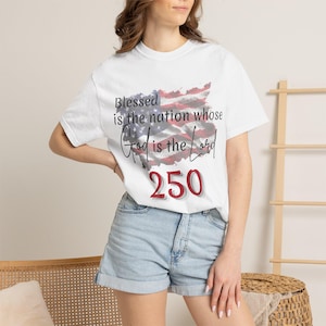 May include: A white short-sleeve t-shirt featuring a distressed American flag graphic with the text "Blessed is the nation whose God is the Lord" and the number "250" in red, white, and blue colors printed on the front of the garment.