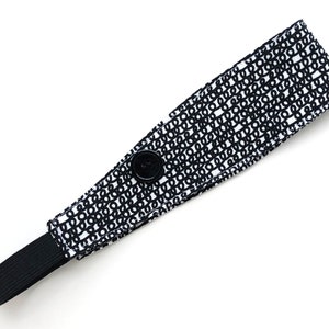 May include: Black and white headband with a button closure and elastic band. The headband has a repeating pattern of black circles on a white background.