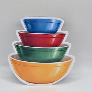 May include: A stack of four colorful mixing bowls in blue, red, green, and yellow. The bowls are nested, with the largest bowl at the bottom and the smallest at the top. The bowls have a glossy finish and a simple, classic design.