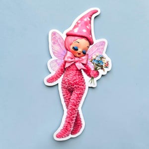 May include: A whimsical sticker of a pink fairy with a matching hat dotted with white circles. The fairy has blue eyes, a pink bow, and delicate wings. She holds a small bouquet of flowers, adding a touch of charm to the design.
