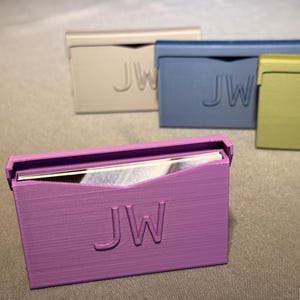 May include: A collection of rectangular cardholders in various colors, including lavender, blue, and green. Each cardholder features the embossed initials "JW" on the front. The lavender cardholder is open, revealing cards inside.