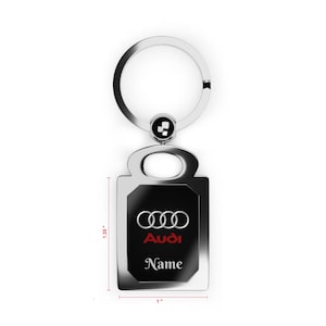 May include: A silver-toned metal keyring featuring a rectangular black insert with the Audi logo and the word Name printed in white and red. The keyring measures 3.43 cm in height and 2.54 cm in width, attached to a circular metal ring.