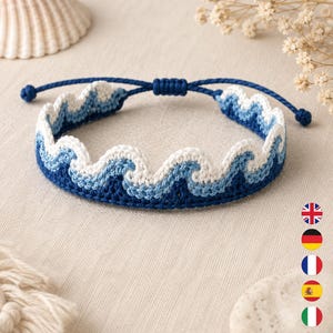 May include: A woven bracelet featuring a repeating wave pattern in shades of dark blue, light blue, and white. The design is crafted with a scalloped top edge and includes an adjustable sliding knot closure made from matching dark blue cord.