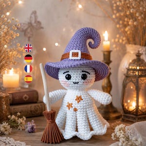 May include: A white crocheted ghost doll wearing a purple pointed hat with a brown band and white buckle. The ghost has black eyes, pink cheeks, and small orange star embroidery on its chest. It holds a small brown broom with a wooden handle.