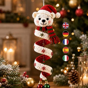 Könnte beinhalten: Ein gehäkelter Eisbär-Anhänger mit einer roten Weihnachtsmütze und einem rot-grün gestreiften Schal. Der Bär ist an einem langen, weißen, spiralförmigen Häkelschwanz befestigt, der mit kleinen roten und grünen gestickten Schneeflocken verziert ist.