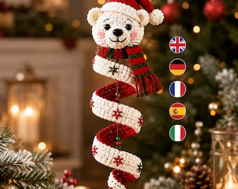 Könnte beinhalten: Ein gehäkelter Eisbär-Anhänger mit einer roten Weihnachtsmütze und einem rot-grün gestreiften Schal. Der Bär ist an einem langen, weißen, spiralförmigen Häkelschwanz befestigt, der mit kleinen roten und grünen gestickten Schneeflocken verziert ist.