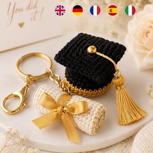 Pode incluir: Um porta-chaves de croché com um barrete de graduação preto com borla dourada e um diploma enrolado de cor creme atado com uma fita dourada. O conjunto está preso a uma argola e um mosquetão de metal de cor dourada.