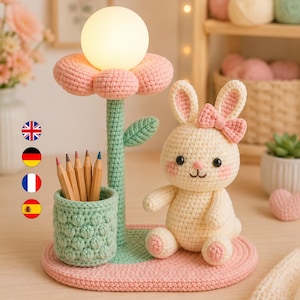 Peut inclure: Un organisateur de bureau en crochet comprenant un lapin crème avec un nœud rose, un porte-crayons vert clair et une lampe en forme de fleur avec une ampoule sphérique blanche lumineuse, sur une base ovale rose plate.