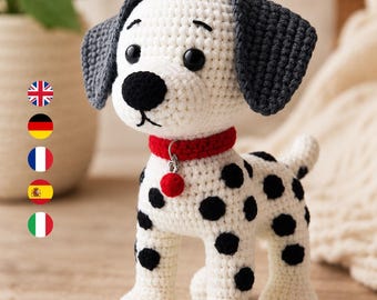 May include: A crocheted Dalmatian dog toy featuring a white body with black spots, dark gray ears, a black nose, and black eyes. The dog wears a bright red collar with a small red pom-pom charm attached to a silver metal ring around its neck.