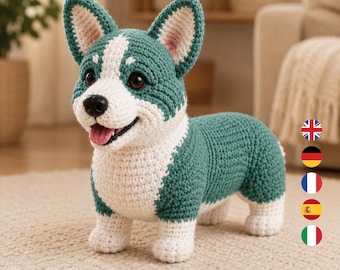 Könnte beinhalten: Ein handgefertigtes Häkel-Corgi-Stofftier in den Farben Petrol und Weiß. Der Hund hat spitze Ohren, dunkle Augen, eine schwarze Nase und ein offenes Maul mit einer rosa Zunge. Der Körper ist mit Garnmaschen strukturiert und steht auf vier Beinen.