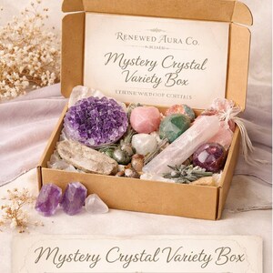 May include: A cardboard box labeled "Mystery Crystal Variety Box" filled with various crystals in shades of purple, pink, green, and clear. The box also contains a variety of crystal shapes and sizes, including clusters, tumbled stones, and raw pieces.