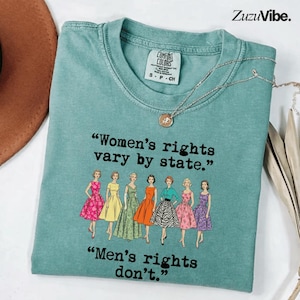 Può includere: Una t-shirt girocollo color verde acqua con una grafica di sette figure illustrate in abiti in stile vintage. Il testo recita: "Women's rights vary by state. Men's rights don't." La maglietta presenta un'etichetta del marchio Comfort Colors.
