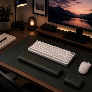 Pode incluir: Um teclado mecânico branco com um botão rotativo prateado, um rato sem fios branco com um logótipo G, um apoio de pulso retangular preto e uma pequena almofada quadrada preta sobre uma grande base preta numa superfície de madeira.