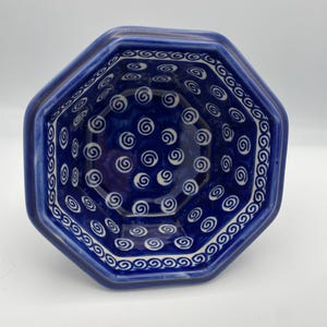 May include: A blue ceramic octagonal bowl with a white swirl pattern. The bowl has a dark blue rim and a lighter blue interior. The white swirl pattern is repeated throughout the bowl's interior and along the rim, creating a decorative design.