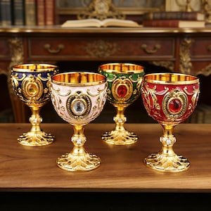 Può includere: Quattro calici decorativi con dettagli dorati. I calici presentano smalto blu, rosa, verde e rosso, ciascuno con un gioiello centrale. Gli steli sono adornati con cristalli e le basi presentano un design floreale dettagliato.