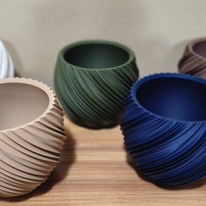 May include: Five decorative planters in various colors: white, tan, green, blue, and brown. Each planter has a unique, textured, spiral design. The planters are arranged on a wooden surface.