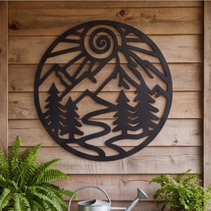 May include: A circular black metal wall art piece featuring a cutout design of a mountain range, a winding path, evergreen trees, and a spiral sun. The silhouette is composed of clean lines and geometric shapes, creating a nature-inspired scene.
