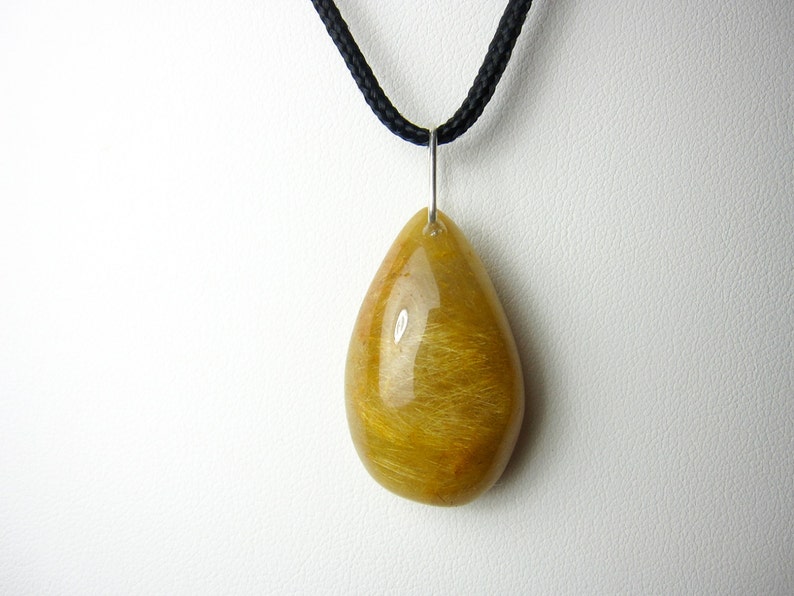 May include: A teardrop-shaped pendant made of golden rutilated quartz, with a silver bail and a black cord.