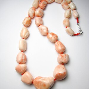 May include: A necklace made of pink coral beads with a silver clasp. The beads are irregular in shape and have a natural, organic look.
