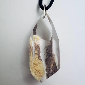 May include: Clear crystal pendant with inclusions of brown and yellow minerals, suspended from a black cord. The crystal is faceted with a pointed bottom and a silver-colored bail.