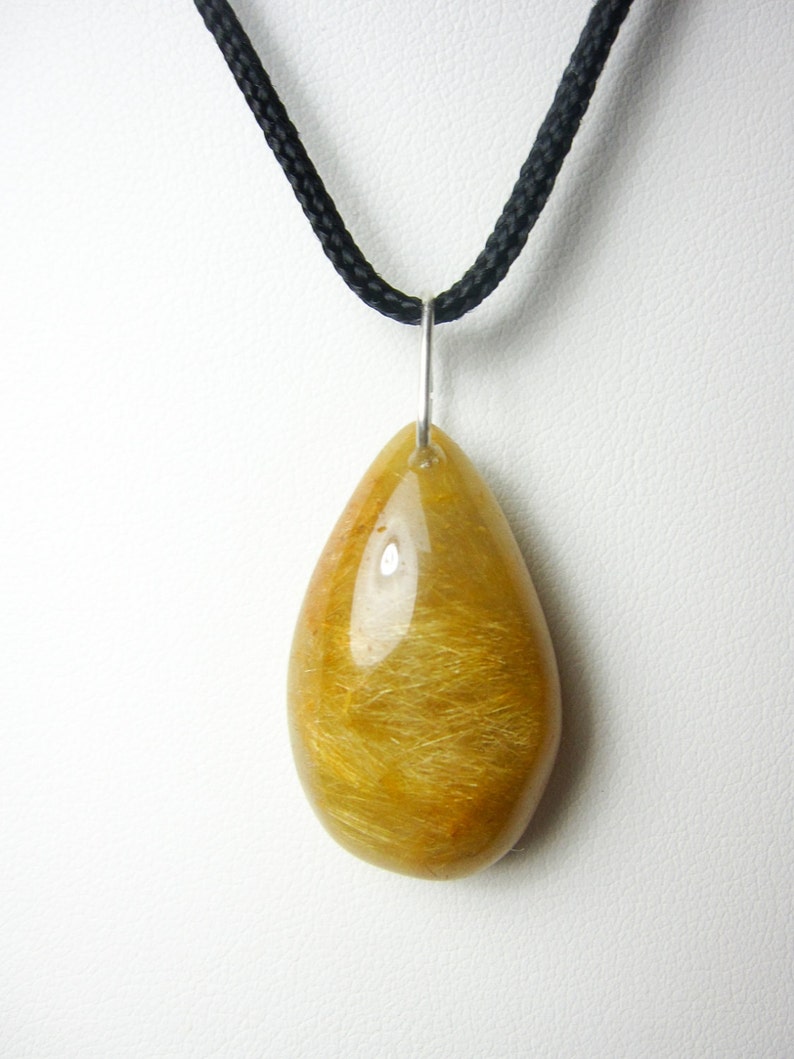 May include: A teardrop-shaped pendant made of golden rutilated quartz, with a silver bail and a black cord necklace.