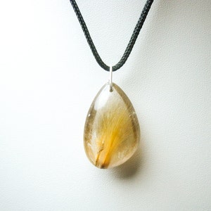 May include: A teardrop-shaped pendant necklace with a clear, golden, and brown crystal. The crystal has a unique, feathery pattern inside. The necklace is on a black cord.