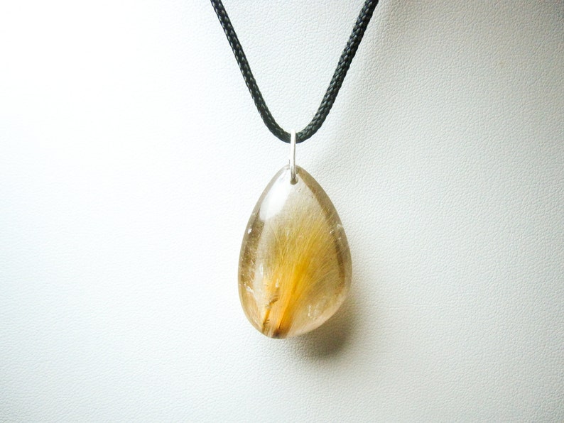 May include: A teardrop-shaped pendant necklace with a clear, golden, and brown crystal. The crystal has a unique, feathery pattern inside. The necklace is on a black cord.