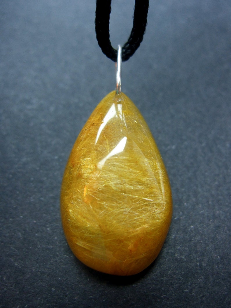 May include: A gold teardrop-shaped pendant with a black cord. The pendant has a translucent, golden color with visible gold flecks.