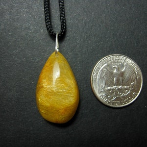 May include: A gold and yellow teardrop-shaped pendant with a silver bail, hanging from a black cord. The pendant is about the size of a US quarter.