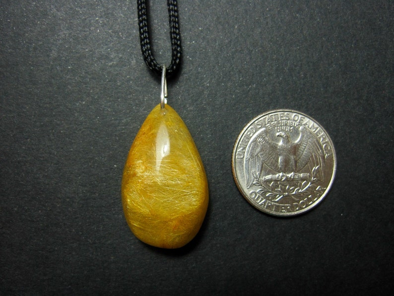 May include: A gold and yellow teardrop-shaped pendant with a silver bail, hanging from a black cord. The pendant is about the size of a US quarter.