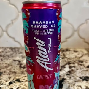 Puede incluir: Una vela cilíndrica en lata, diseñada para parecerse a una lata de bebida energética Alani Nu Hawaiian Shaved Ice. La lata es principalmente roja y morada, con detalles turquesa y blancos, y presenta el texto "Hawaiian Shaved Ice" y "Energy".