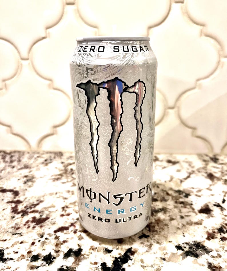 Pu&ograve; includere: Una lattina d'argento di Monster Energy Zero Ultra con il logo ad artiglio del marchio. La lattina presenta la scritta "ZERO SUGAR" in alto e "MONSTER ENERGY ZERO ULTRA" sul davanti. La lattina &egrave; su un piano di lavoro maculato.