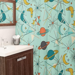 May include: A teal shower curtain with a retro space-themed pattern. The design includes planets, moons, stars, boomerangs, and geometric shapes in orange, yellow, and teal. The curtain hangs in a bathroom with a wooden vanity and a white countertop.