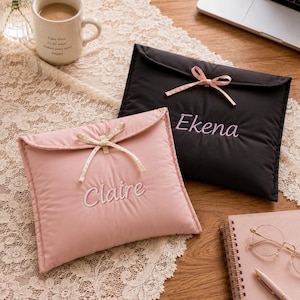 May include: Two rectangular quilted pouches with envelope-style flaps and ribbon ties. One pouch is light pink with the name Claire embroidered in white, and the other is black with the name Ekena embroidered in light pink thread.