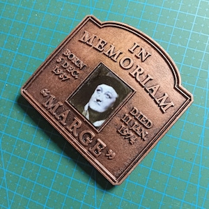 May include: A brown wooden plaque with a photo of a person and the text "IN MEMORIAM BORN 5 DEC 1937 DIED 11 JAN 1974 "MARGE""