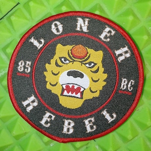 May include: Black and red embroidered patch featuring a yellow tiger head and the text "LONER REBEL 85 BC" in white.