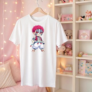May include: White t-shirt featuring a colorful anime character illustration. The character has pink hair, blue and white striped markings, and is dressed in a red vest and white pants. The shirt is hanging on a wooden hanger.