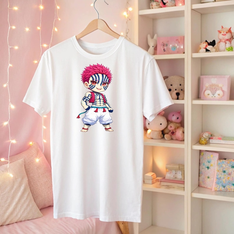 May include: White t-shirt featuring a colorful anime character illustration. The character has pink hair, blue and white striped markings, and is dressed in a red vest and white pants. The shirt is hanging on a wooden hanger.