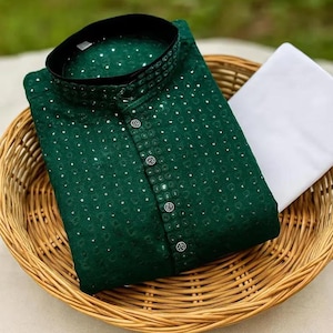 May include: Emerald green kurta with a mandarin collar and sequin detailing. The kurta features a button-down front and is paired with white pants, presented in a woven basket. The outfit is suitable for festive occasions.