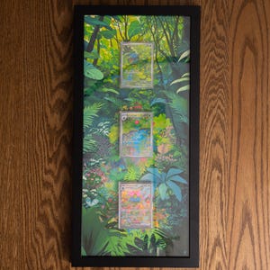 May include: A rectangular black frame containing three trading cards displayed vertically against a vibrant jungle-themed background. The artwork features lush green foliage, tropical plants, and colourful flowers, with the cards centred in the frame.